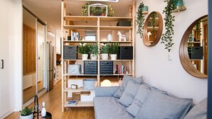 A modern living room with a grey sofa, wooden shelving with plants, and a large mirror. - Phaedrus Living: Seaside Luxury Flat Athina 109 (Paphos)