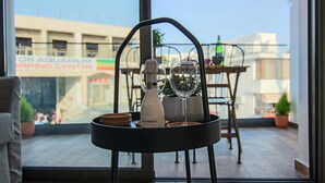 A balcony with a table holding a bottle and glasses, a chair, and a view of a building with a sign. - Phaedrus Living: Seaside Luxury Flat Athina 109 (Paphos)