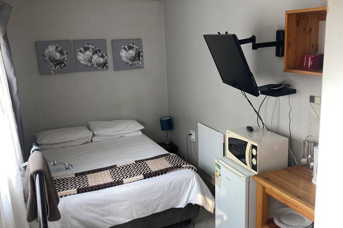 A bedroom with a bed, a desk with a microwave, a lamp, and three wall-mounted pictures.