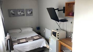 A bedroom with a bed, a desk with a microwave, a lamp, and three wall-mounted pictures.