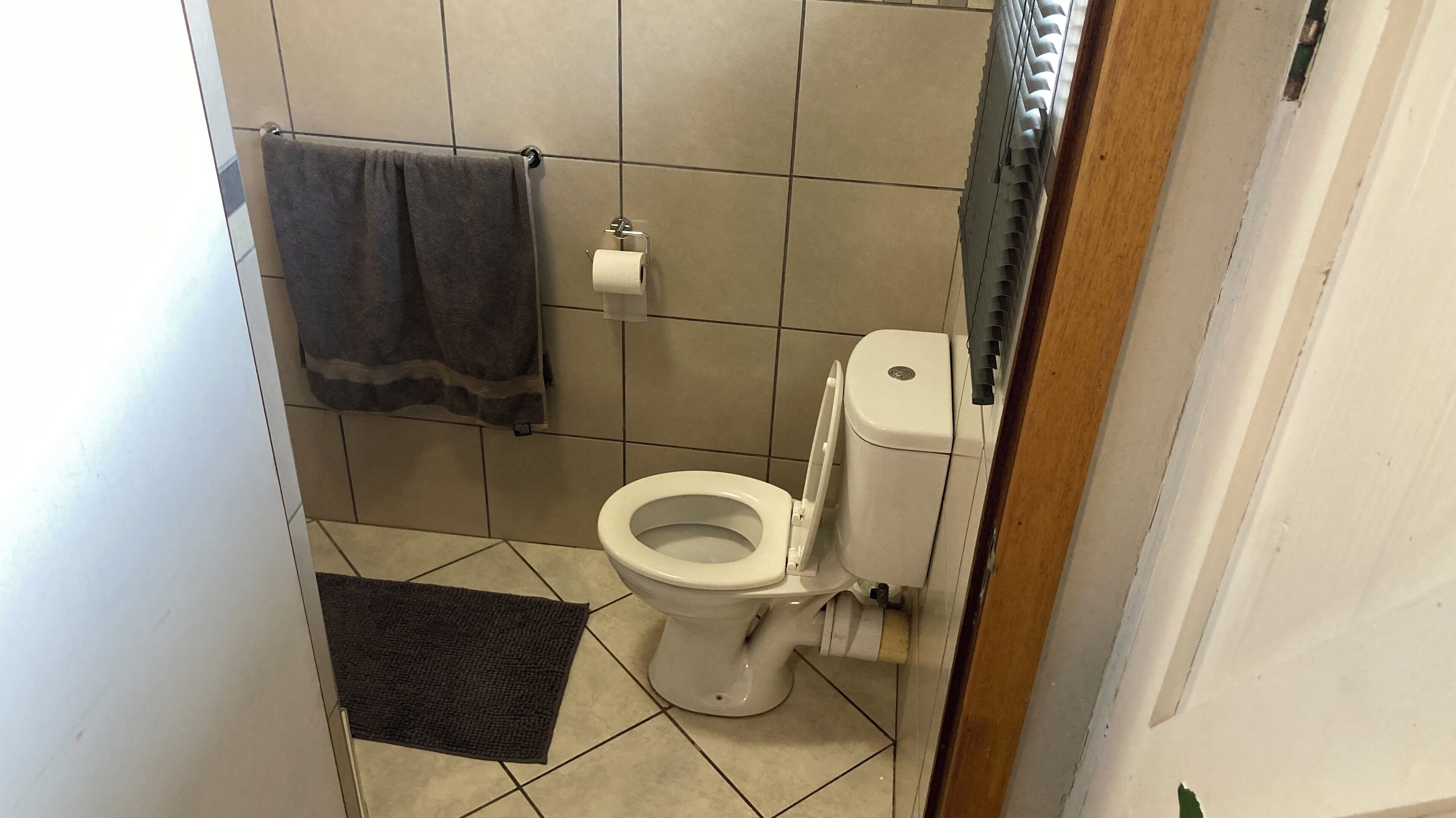 Un baño con un inodoro, una toalla colgada en un perchero y una alfombra pequeña en el suelo.