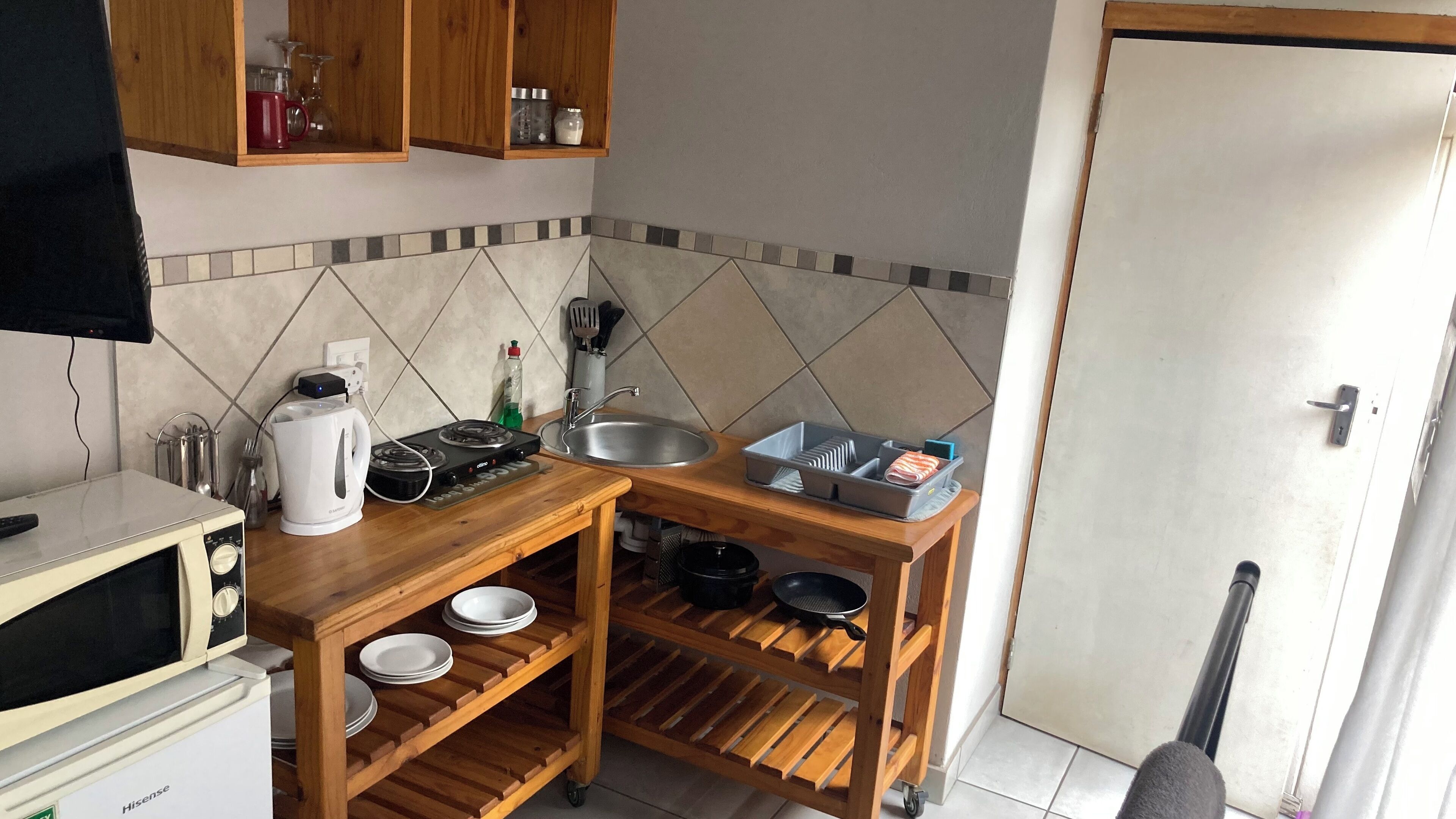 A compact kitchen with a microwave, stove, sink, and wooden shelves.