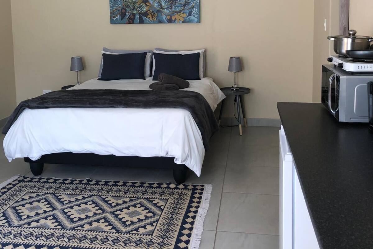 A bedroom with a bed, bedside lamps, a painting, a microwave, and a small table.