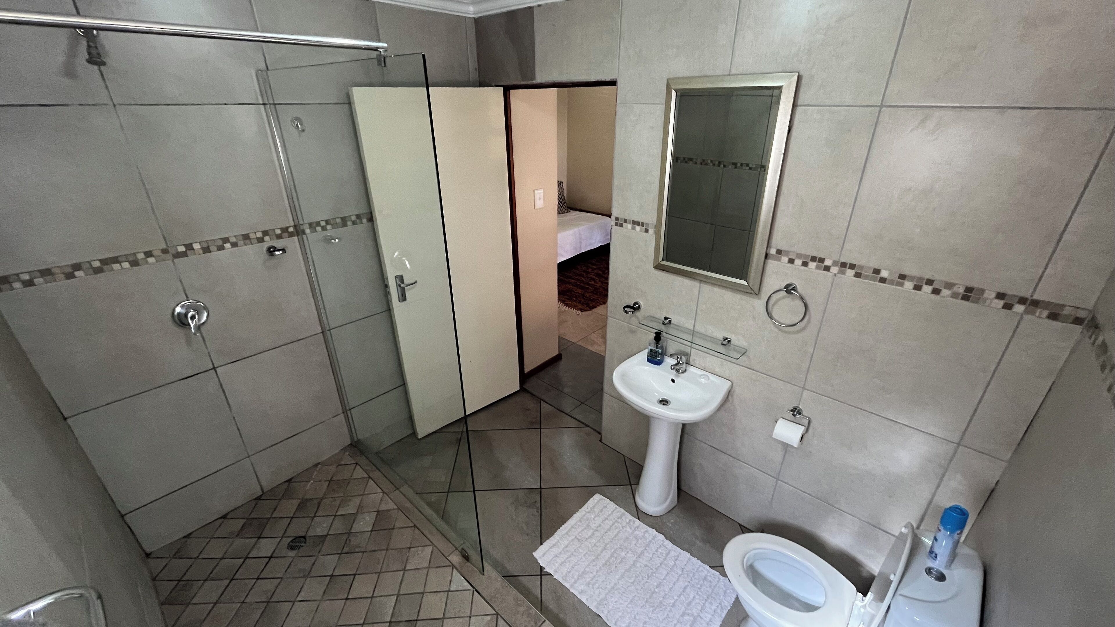 A bathroom with a shower, toilet, sink, and a mirror.
