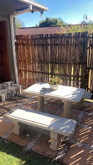 Un patio al aire libre con una mesa y banca, rodeado por una cerca decorativa y un jardín.