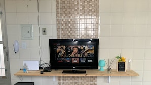 Un salón moderno con un televisor de pantalla plana sobre un estante de madera, dos otomanas azules y un revestimiento de azulejos.