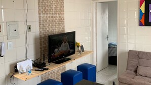 Una sala de estar moderna con televisor, otomanas azules, pared de azulejos color beige y una puerta que da a otra habitación.