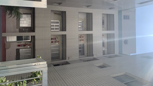 Un edificio moderno con múltiples ventanas, algunas con barrotes, y piso de baldosas.