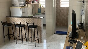 Un espacio habitable compacto con kitchenette, zona de comedor con taburetes de bar, televisión y una pequeña mesa con un cartel de pizarra.