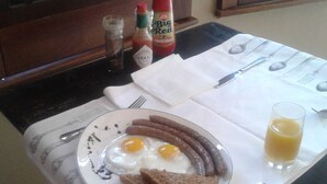 A breakfast table with a plate of eggs, sausages, toast, and a glass of orange juice. There are condiments and cutlery on the table. - Tumbleweeds (Chartwell)