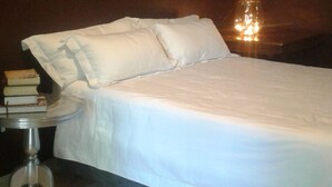 A neatly made bed with white linens, a bedside table with books, and two framed pictures on the wall. - Tumbleweeds (Chartwell)