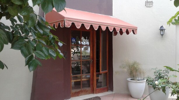 A small building with a red awning, a large potted plant, and a tiled patio area. - Tumbleweeds (Chartwell)