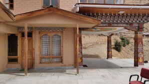 A traditional building with a wooden entrance, a covered porch with patterned columns, and a stone wall in the background. - Thori Resort (Thimphu)