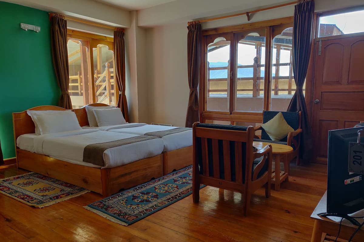 A room with a wooden bed, a chair, a television, and a view of the outdoors through large windows.
