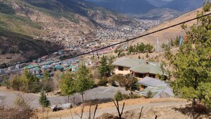 A town nestled in a valley with a mountain backdrop, featuring a mix of residential and commercial buildings, and a prominent cable car line. - Thori Resort (Thimphu)