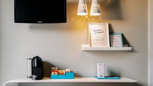 Ein modernes Wohnzimmer mit Flachbildfernseher, einer Kaffeemaschine, einem Minikühlschrank, einem roten Hocker und einem an der Wand befestigten Regal mit einem Willkommensschild und einem gerahmten Zertifikat.