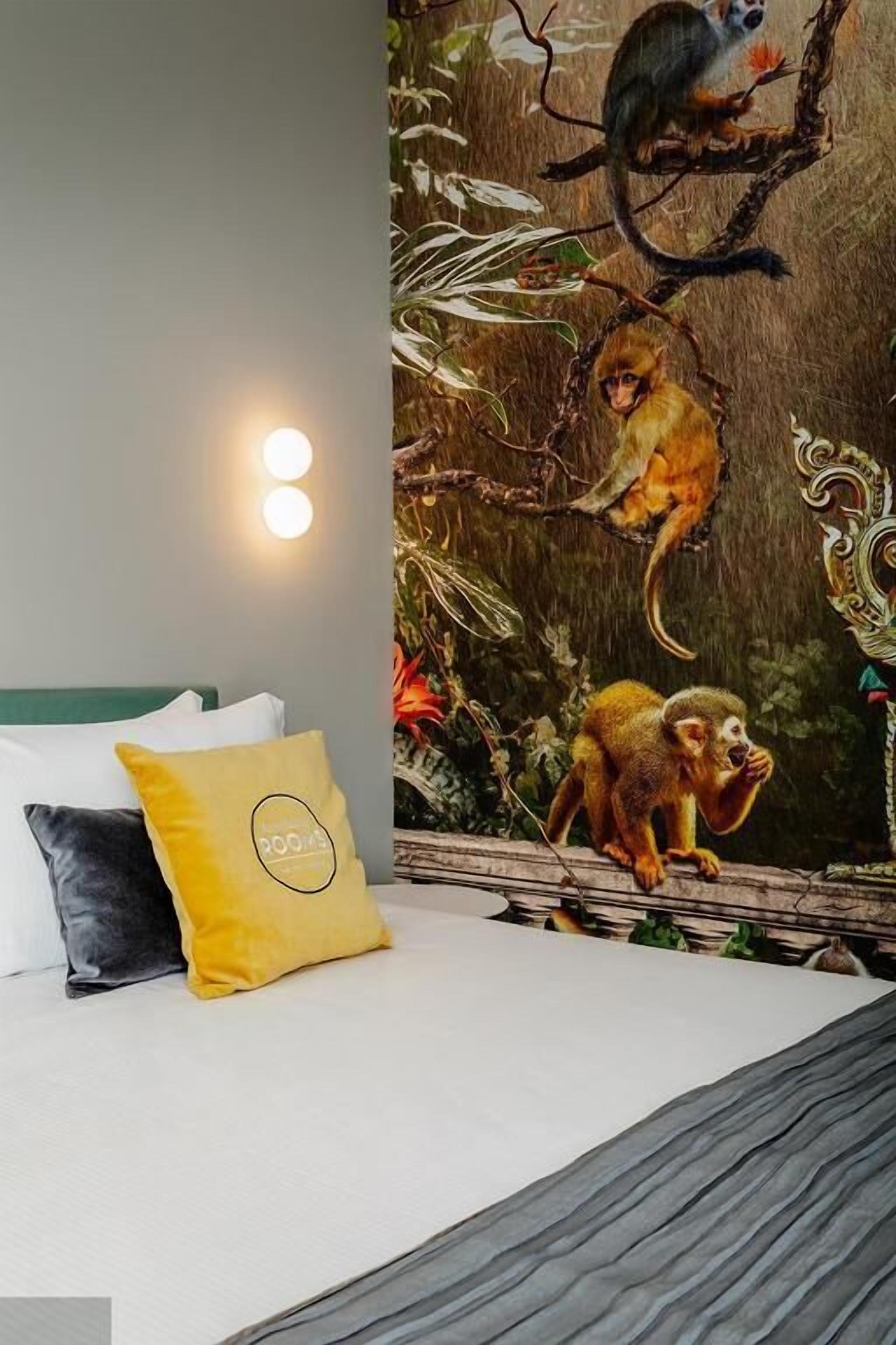 A bedroom with a bed, pillows, and a wall mural of monkeys on a tree branch.