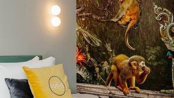 A bedroom with a bed, pillows, and a wall mural of monkeys on a tree branch.