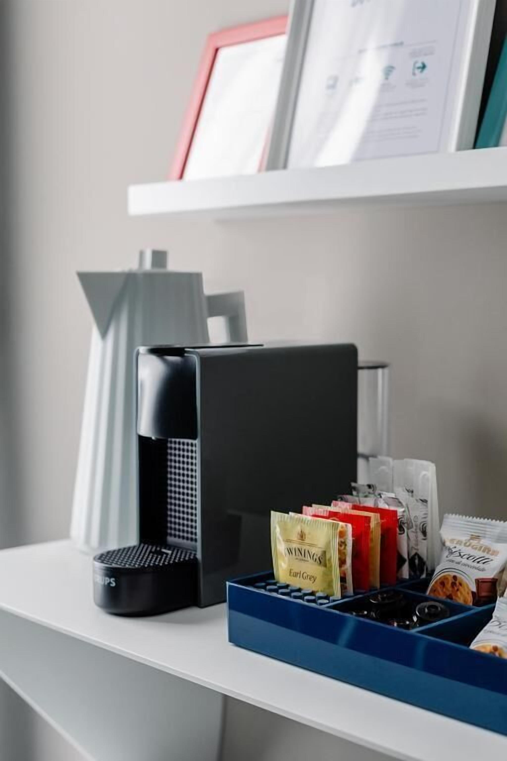 A coffee machine, a blue tray with snacks, and a framed menu on a white counter.