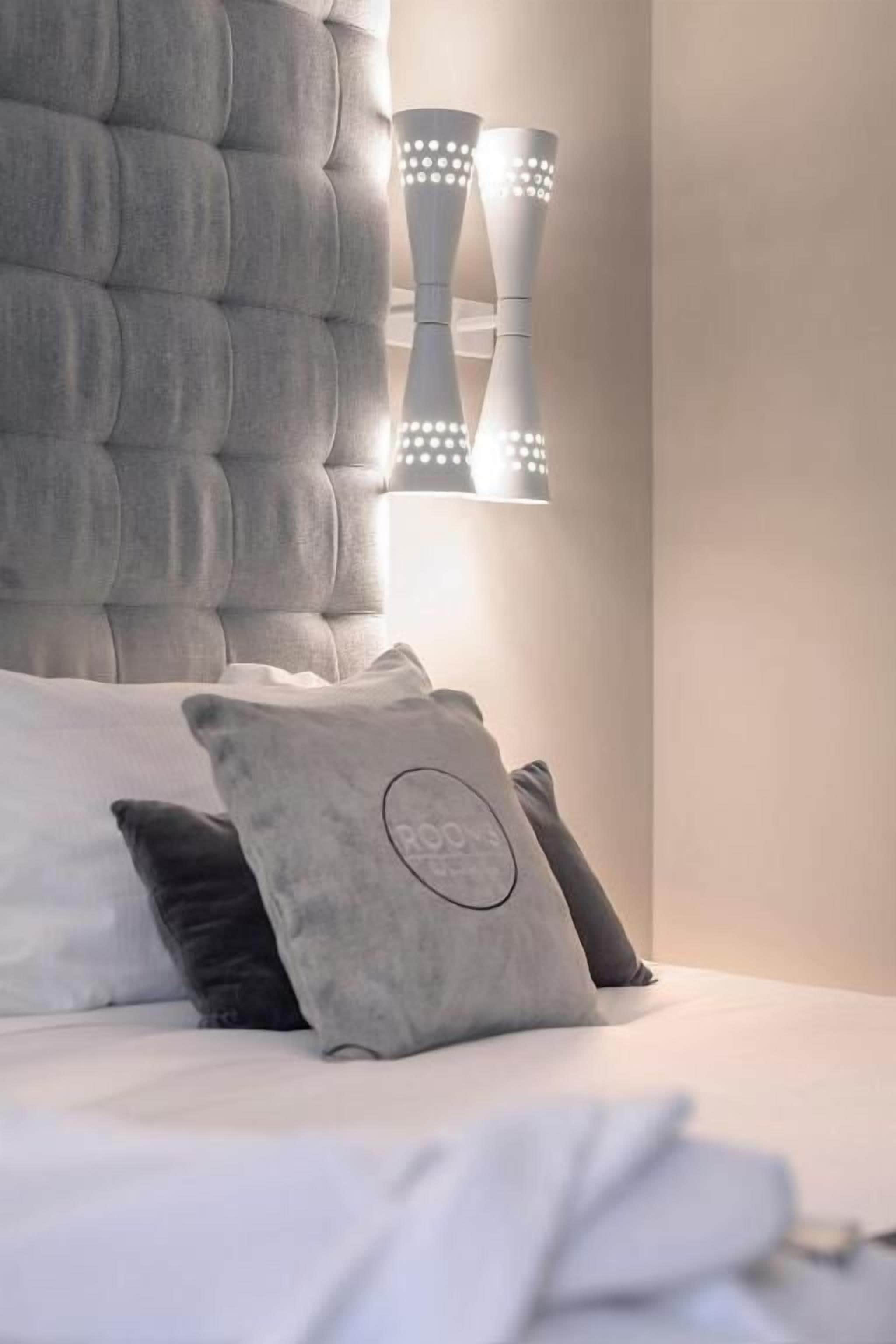 A bedroom with a tufted headboard, a bed with white bedding, and two wall-mounted light fixtures.