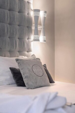 Une chambre à coucher avec une tête de lit capitonnée, un lit recouvert de linge de lit blanc et deux appliques murales.
