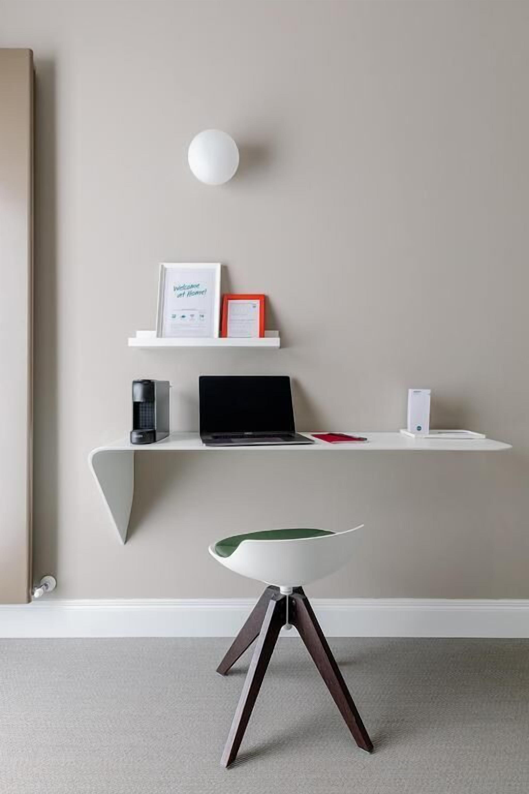 A modern workspace with a laptop, a coffee machine, and a speaker on a white desk against a plain wall.