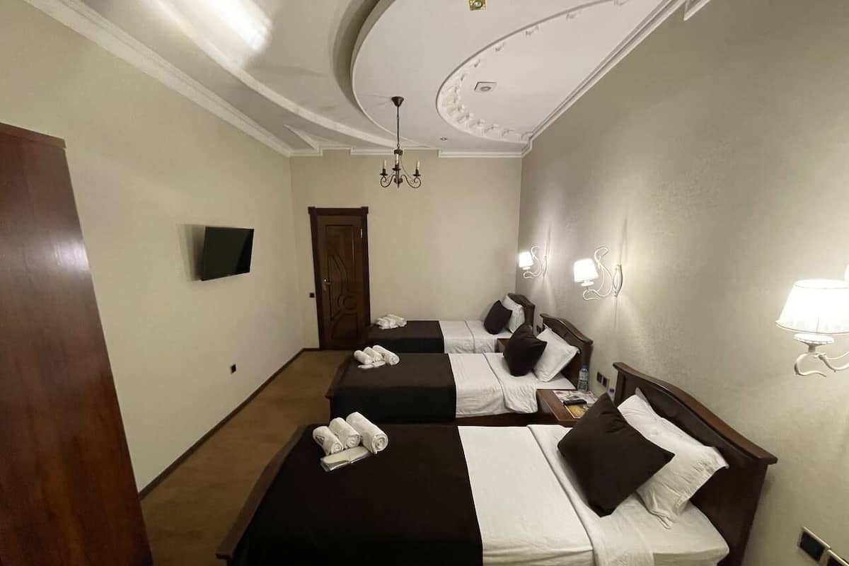 A hotel room with three beds, a chandelier, a flat-screen TV, and a door.