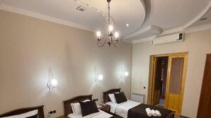 Een hotelkamer met drie bedden, een kroonluchter, wandlampen en een radiator.
