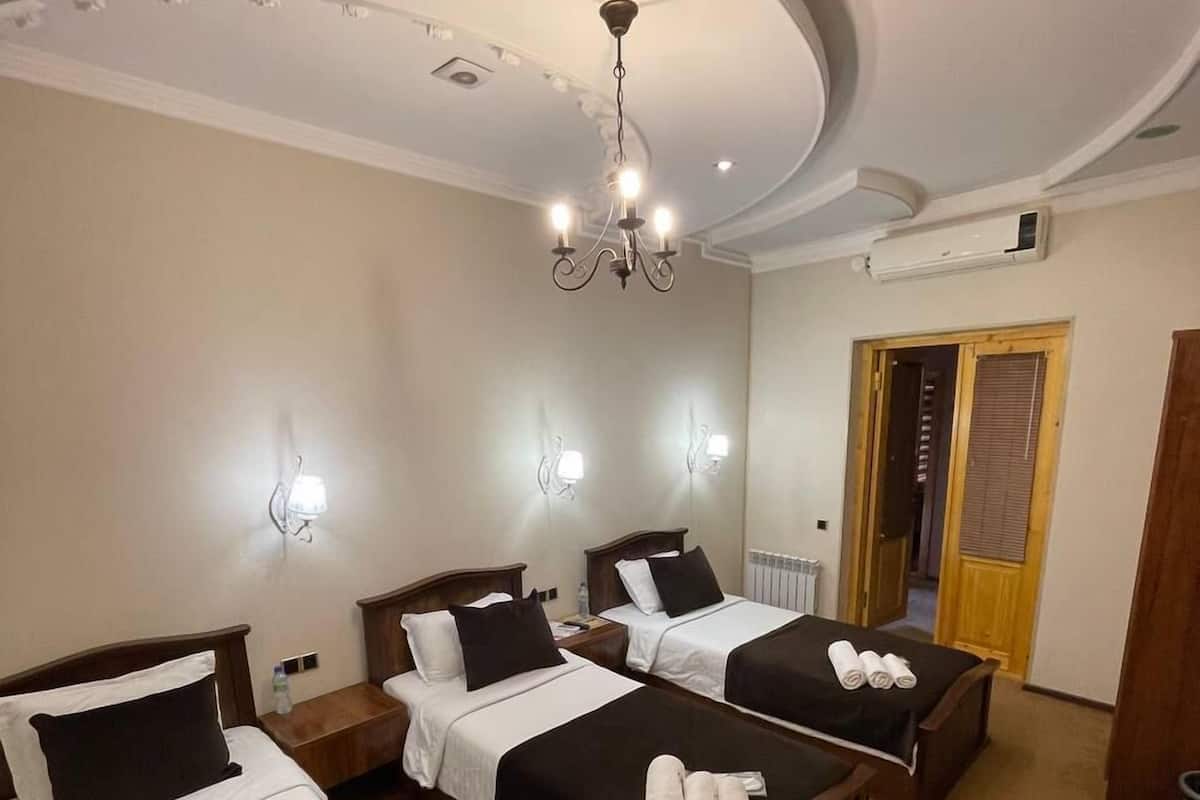 A hotel room with three beds, a chandelier, wall sconces, and a radiator.
