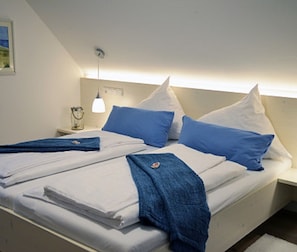 A neatly made bed with white and blue bedding, a bedside lamp, and a small table with a glass container. - Quartier restaurant Zum Hannes (Winterbach)