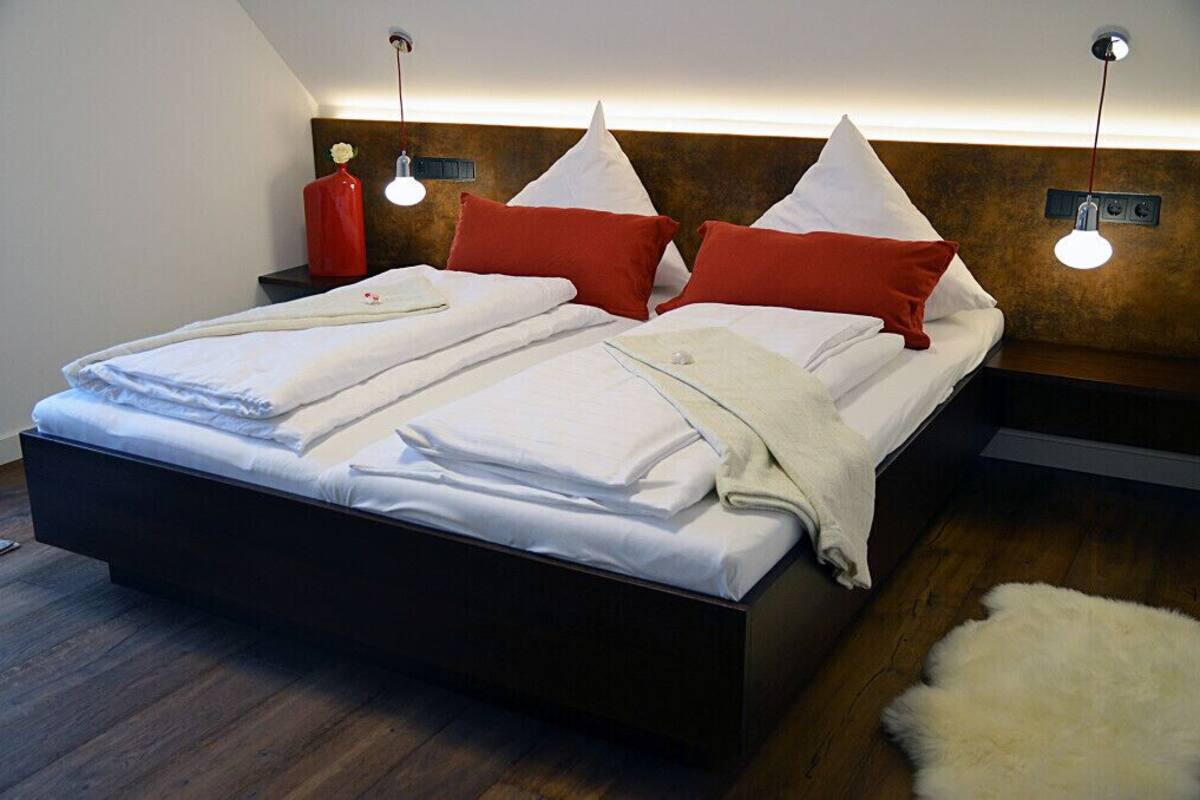 A modern bedroom with a large bed, two bedside tables, and a headboard with integrated lighting.