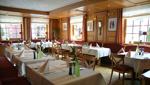 A restaurant with multiple tables set for dining, wooden paneling on the walls, and large windows allowing natural light. - Quartier restaurant Zum Hannes (Winterbach)