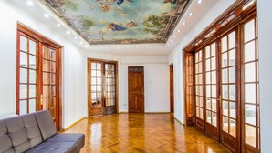 A spacious hallway with wooden floors and large windows, leading to a room with a ceiling mural.
