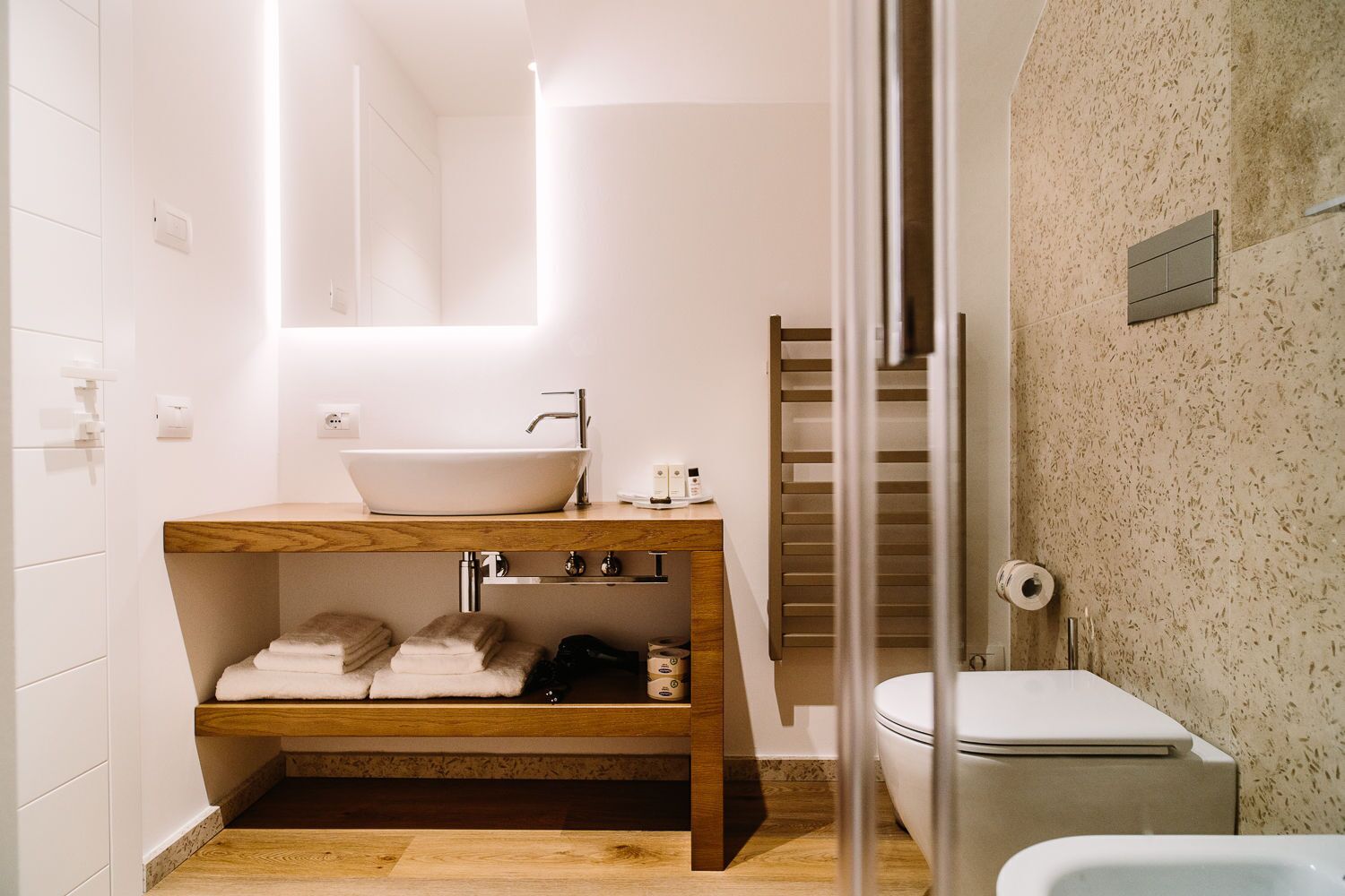 A modern bathroom with a wooden vanity, a white sink, and a toilet.