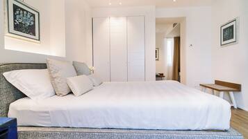 A bedroom with a large bed, a wardrobe, a small table, and a chair.