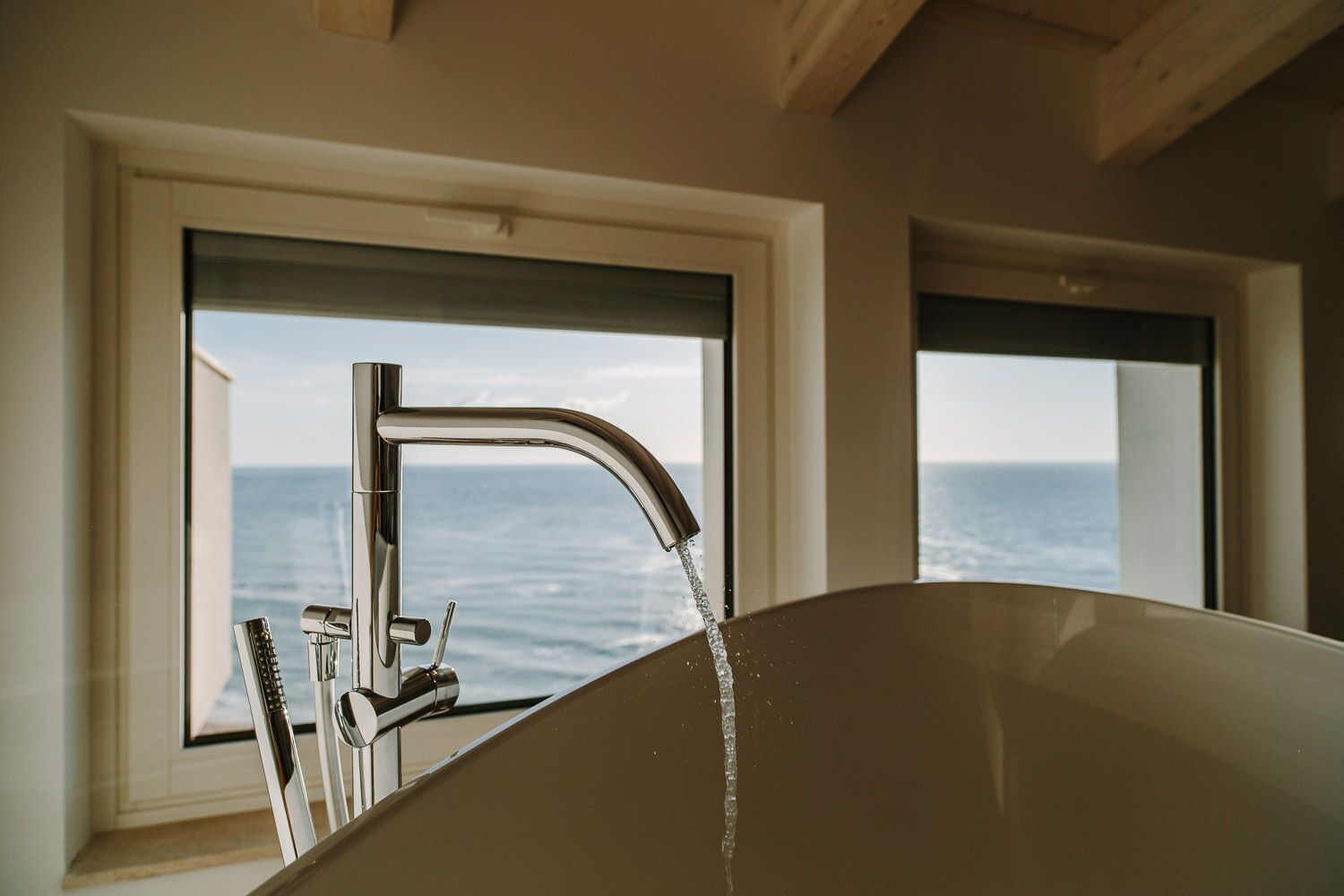 Uma casa de banho com banheira, uma torneira moderna e vista para o oceano através de uma janela.