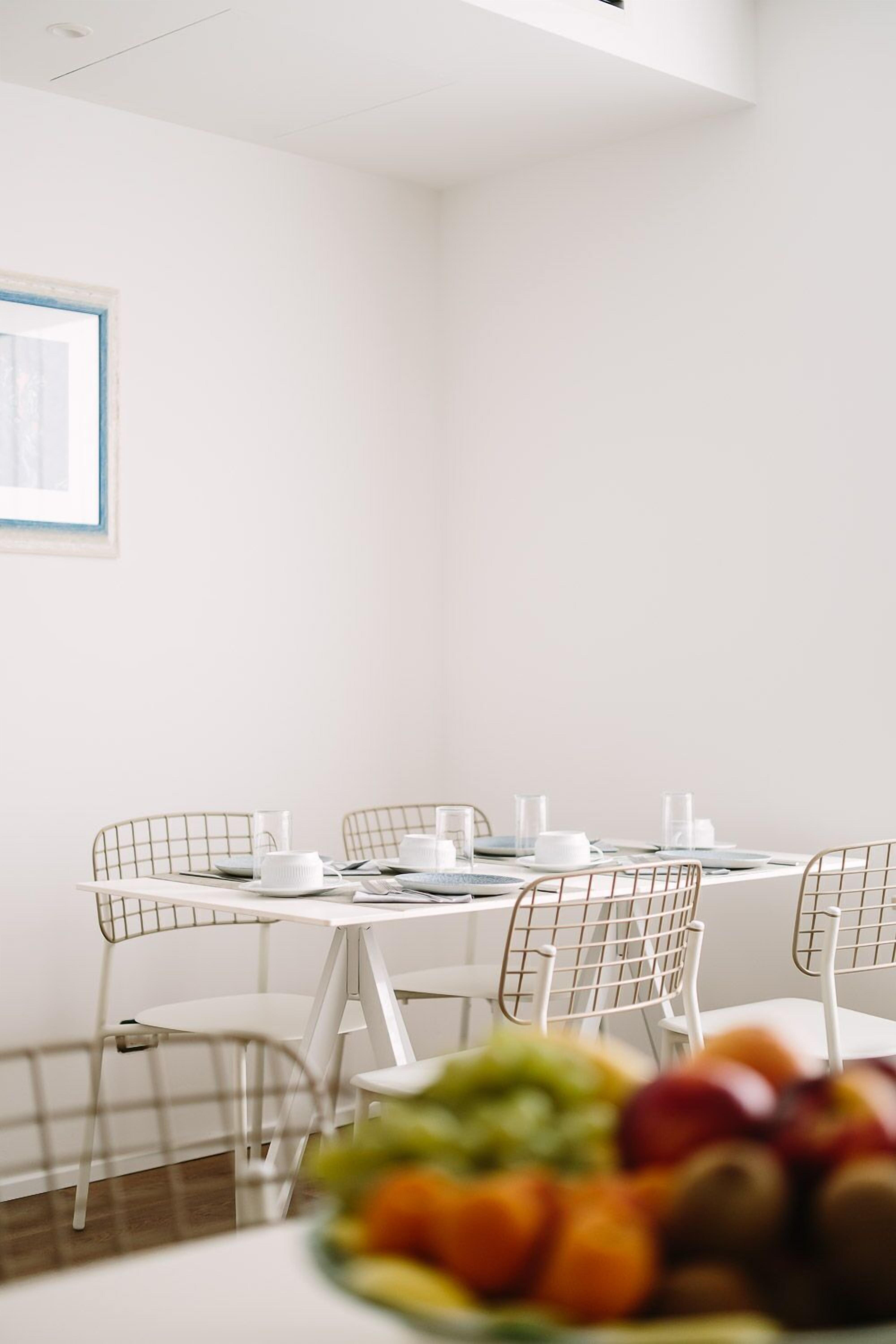 A dining area with a white table set for four, surrounded by white wire chairs.