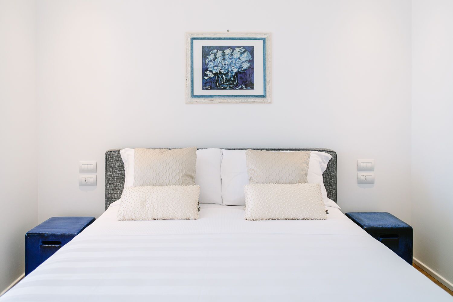 A double bed with white bedding, two white pillows, and a framed painting above it.