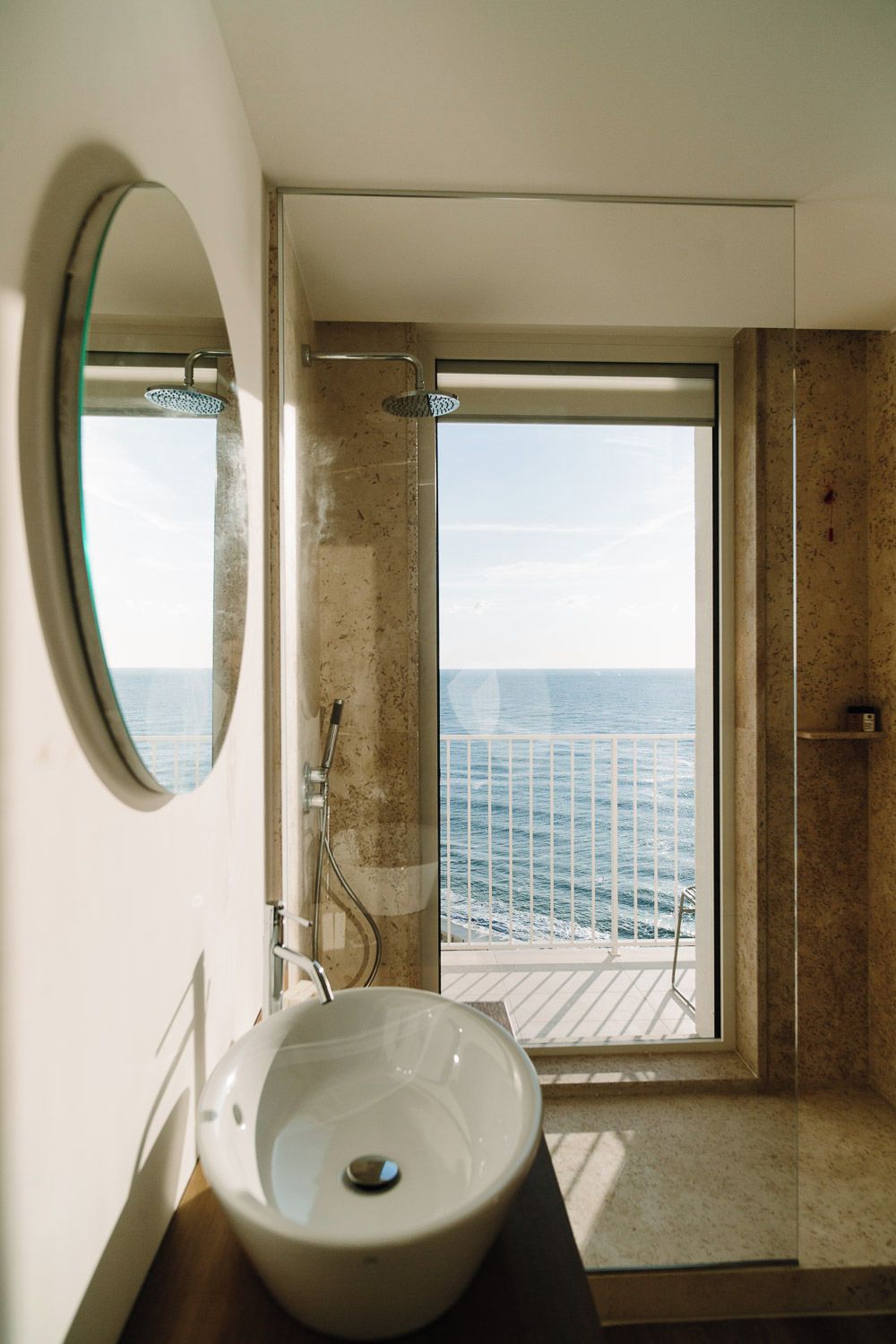 Un bagno con una grande finestra, uno specchio rotondo e un lavandino.