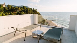 A balcony with two sun loungers and a small table, overlooking a beach and a forested hillside. - Numa Hotel (Numana)