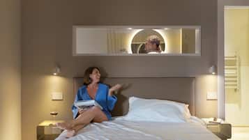 A person sitting on a bed in a hotel room with a nightstand, a bedside table, and a wall-mounted mirror.