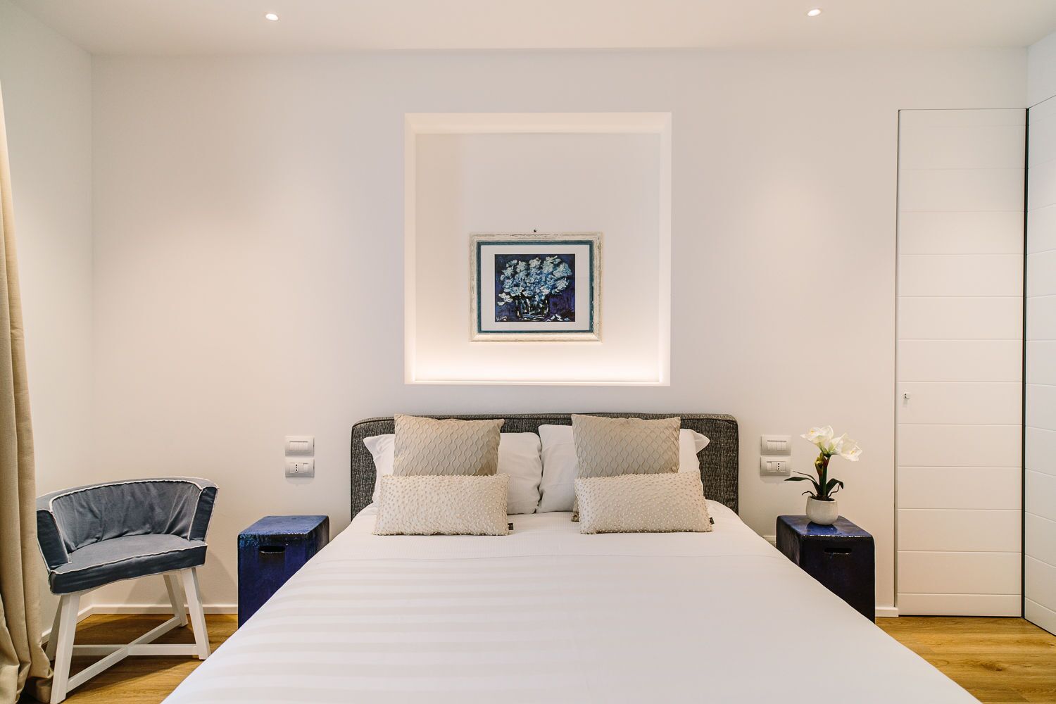 Un dormitorio moderno con una cama grande, una silla, una mesita de noche y un cuadro enmarcado en la pared.