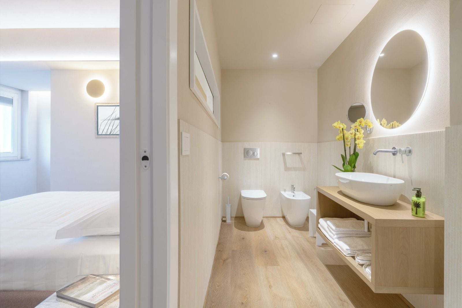 Une salle de bain moderne avec un grand miroir ovale, un lavabo blanc et deux toilettes.
