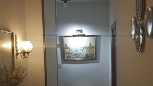 A hallway with a wooden dresser, a vase of flowers, a wall-mounted light fixture, a framed painting, and a radiator. - Hotel Andalucia (Cazorla)