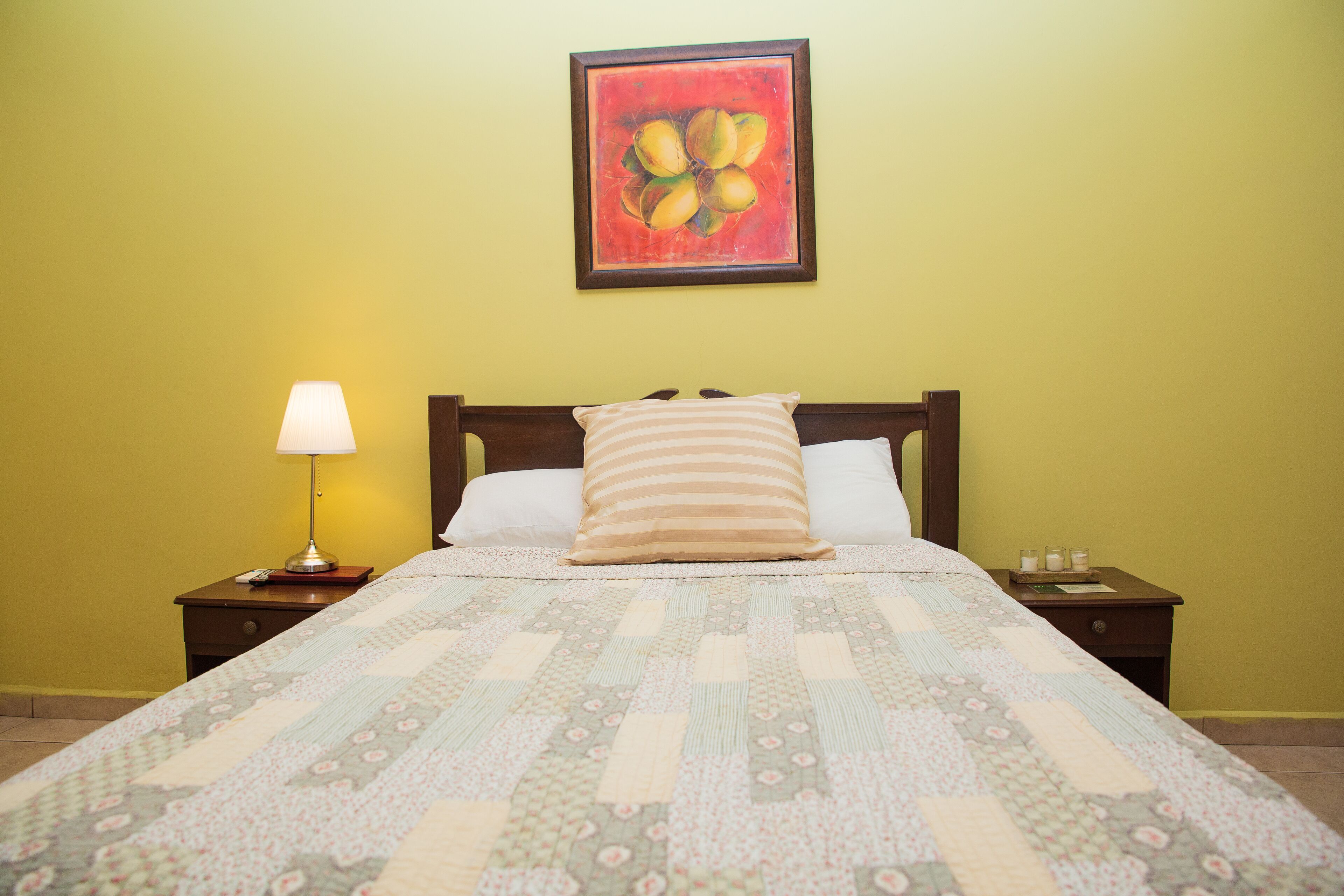 A neatly made bed with a floral quilt, a bedside lamp, and a framed painting on the wall.