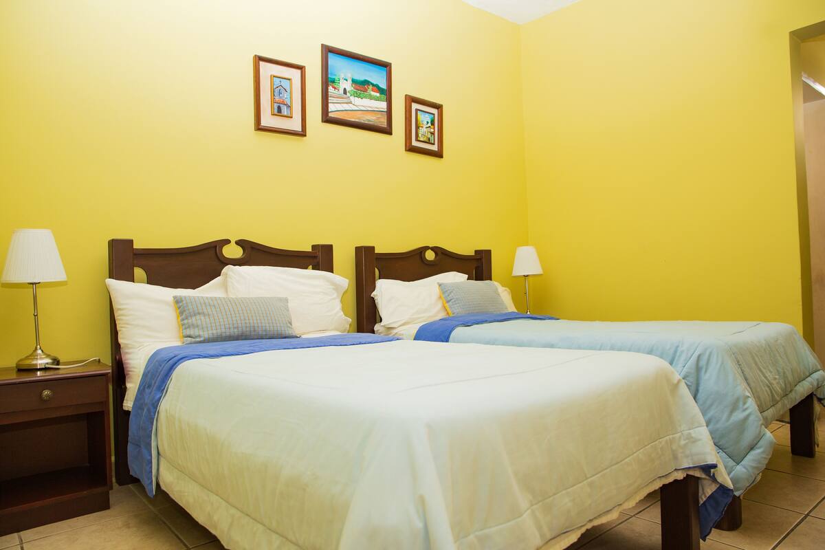 Una habitación de hotel con dos camas, una mesita de noche y una pared decorada con tres cuadros.