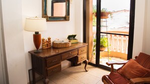 Una habitación con escritorio de madera, lámpara, espejo y puerta de cristal corredera que da a un área exterior con balcón.