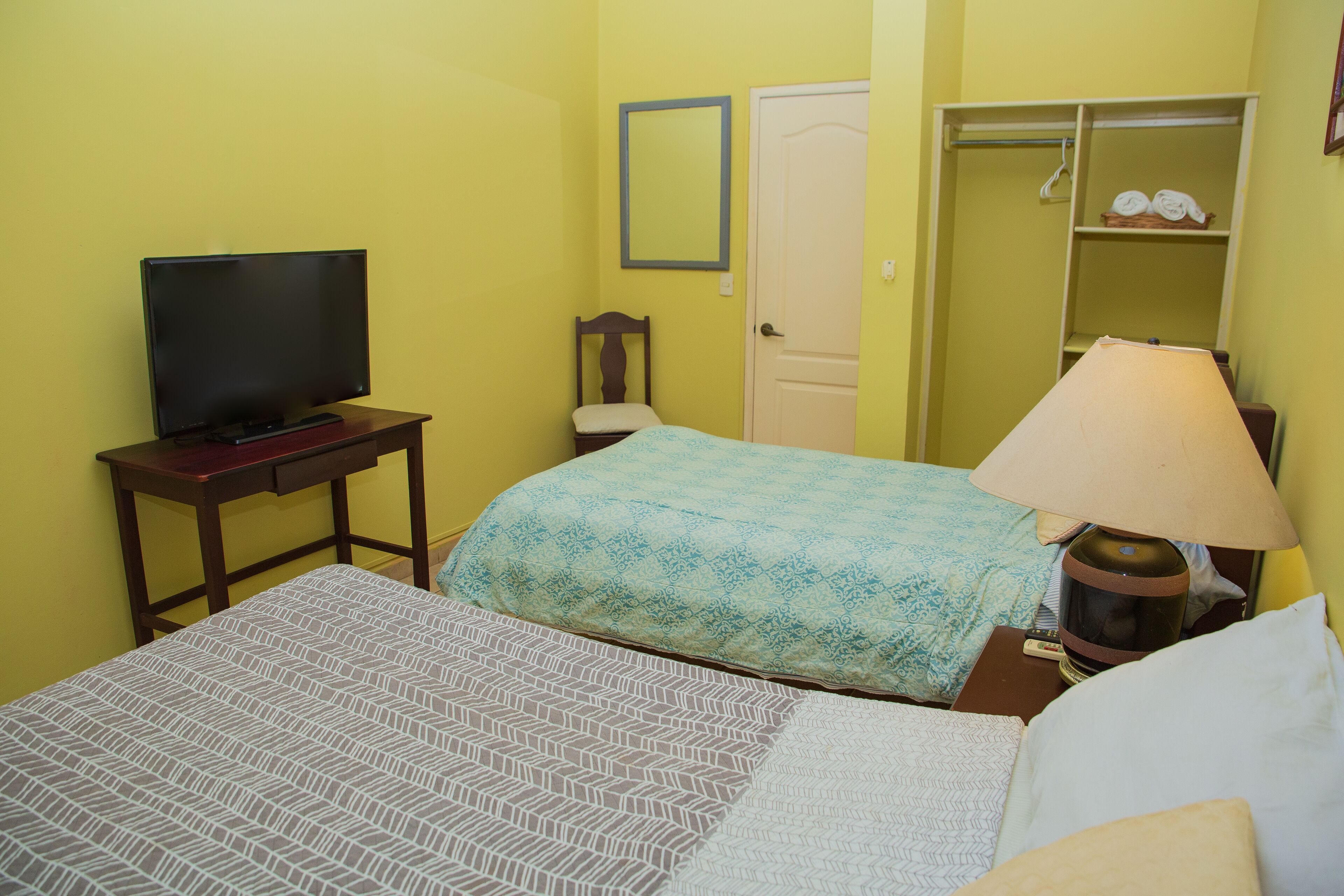 Una camera d'albergo con un letto, una televisione su un tavolino in legno, una lampada, un armadio e uno specchio a parete.