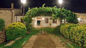A stone building with a vine-covered archway, a paved pathway, and two street lamps. - Aranceto Turismo Rurale (Syracuse)