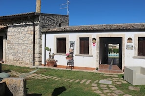 A building with a stone facade, a tiled roof, and a small garden area with potted plants and a ladder. - Aranceto Turismo Rurale (Syracuse)